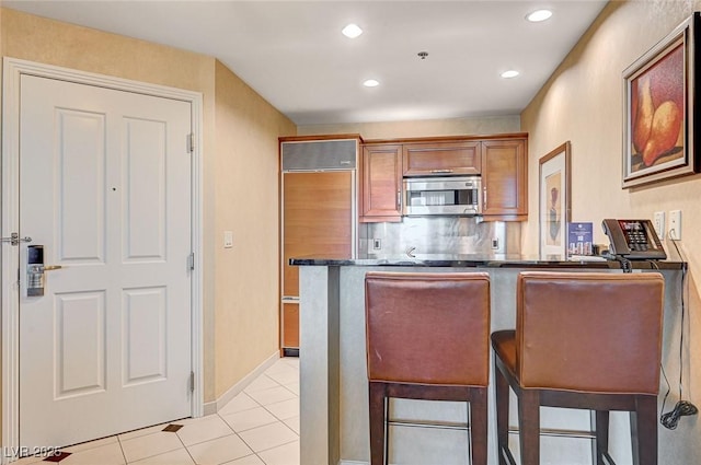 kitchen with paneled fridge, light tile patterned floors, kitchen peninsula, and a kitchen breakfast bar