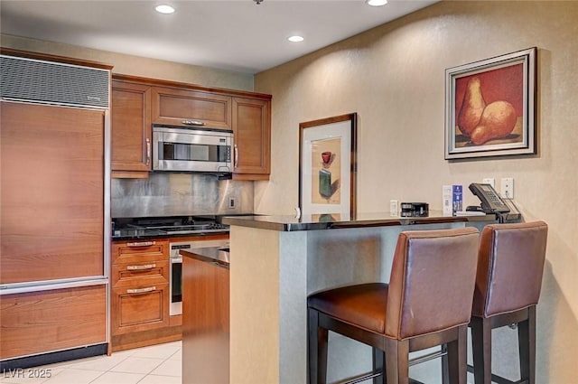 kitchen featuring a breakfast bar area, light tile patterned flooring, tasteful backsplash, and stainless steel appliances