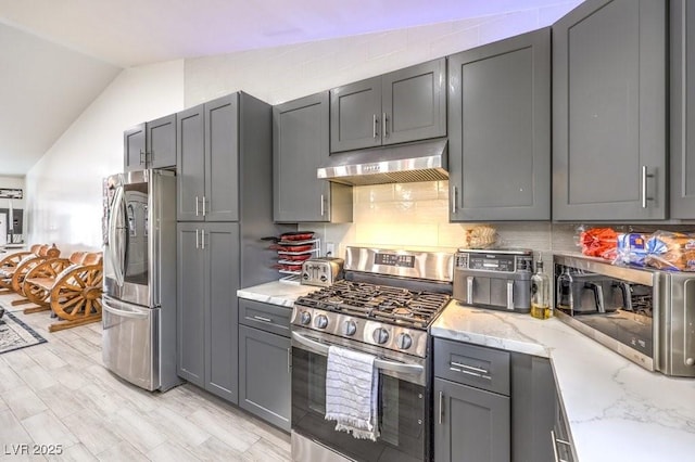 kitchen featuring lofted ceiling, light stone countertops, gray cabinets, and stainless steel appliances