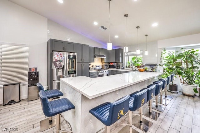 kitchen with a kitchen bar, kitchen peninsula, appliances with stainless steel finishes, hanging light fixtures, and vaulted ceiling