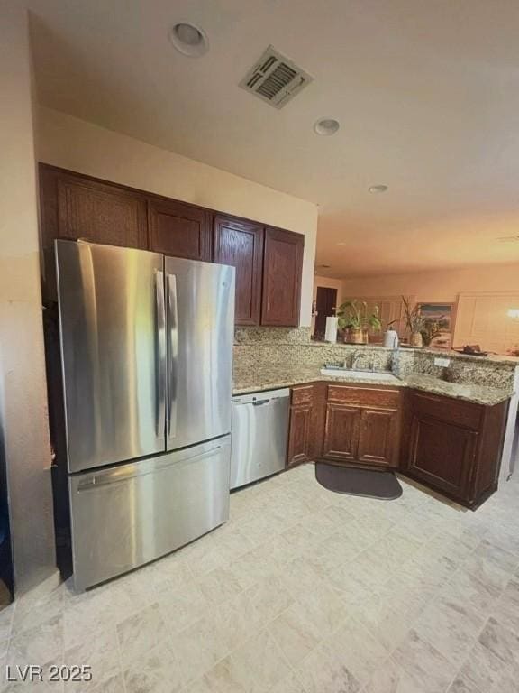 kitchen featuring light stone countertops, sink, kitchen peninsula, backsplash, and stainless steel appliances