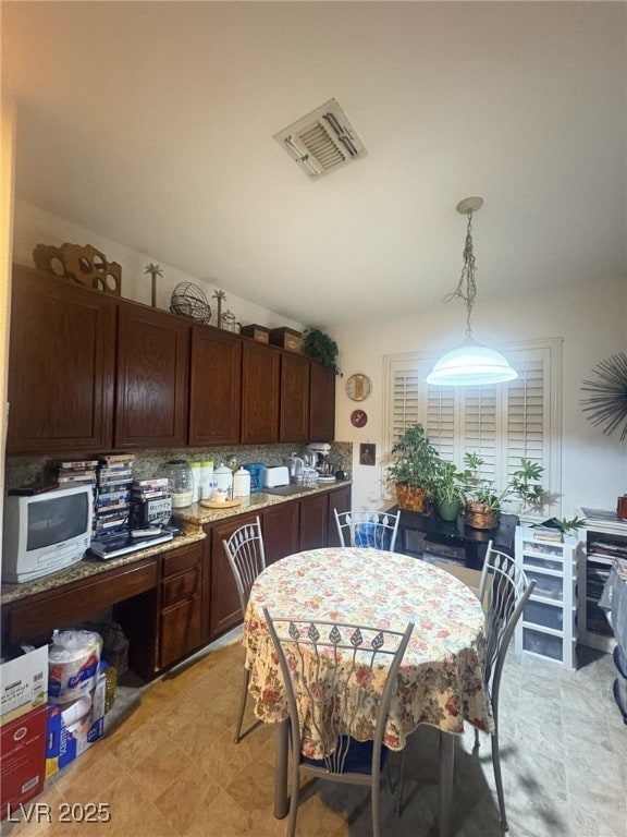 kitchen featuring decorative light fixtures, light stone counters, dark brown cabinets, and tasteful backsplash