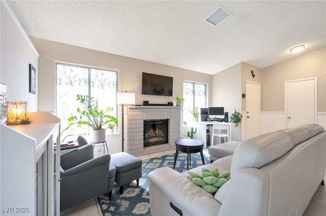 living room with vaulted ceiling, a brick fireplace, light tile patterned floors, and a textured ceiling