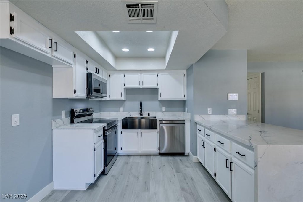 kitchen featuring a raised ceiling, white cabinets, appliances with stainless steel finishes, and sink