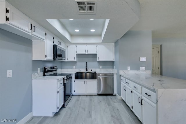 kitchen featuring a raised ceiling, white cabinets, appliances with stainless steel finishes, and sink