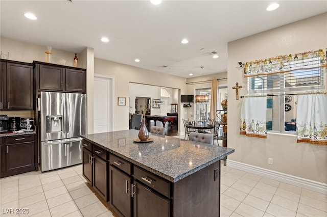 kitchen featuring light tile patterned floors, stainless steel fridge, dark brown cabinetry, and dark stone counters