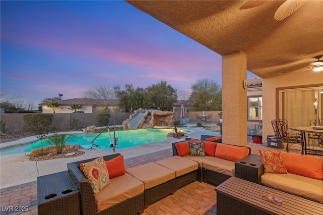 pool at dusk with a patio area, outdoor lounge area, ceiling fan, and a water slide