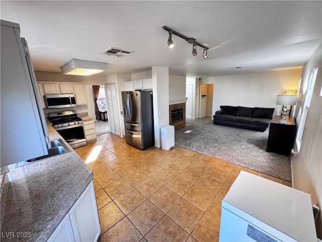 kitchen featuring a tile fireplace, appliances with stainless steel finishes, white cabinetry, rail lighting, and light colored carpet