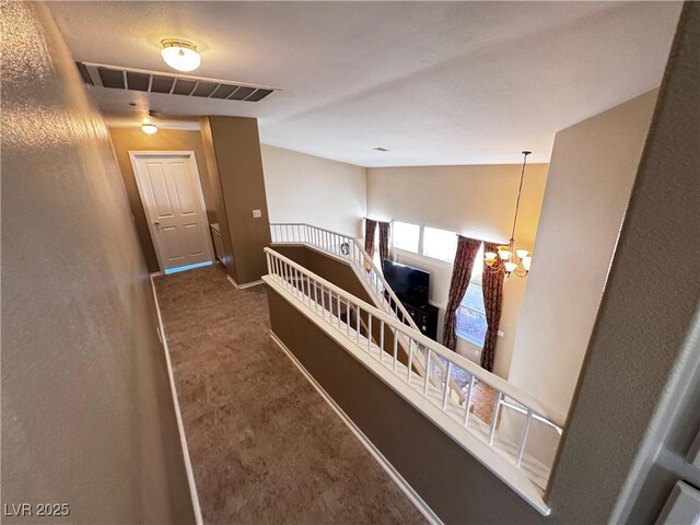 hallway with dark carpet and a notable chandelier