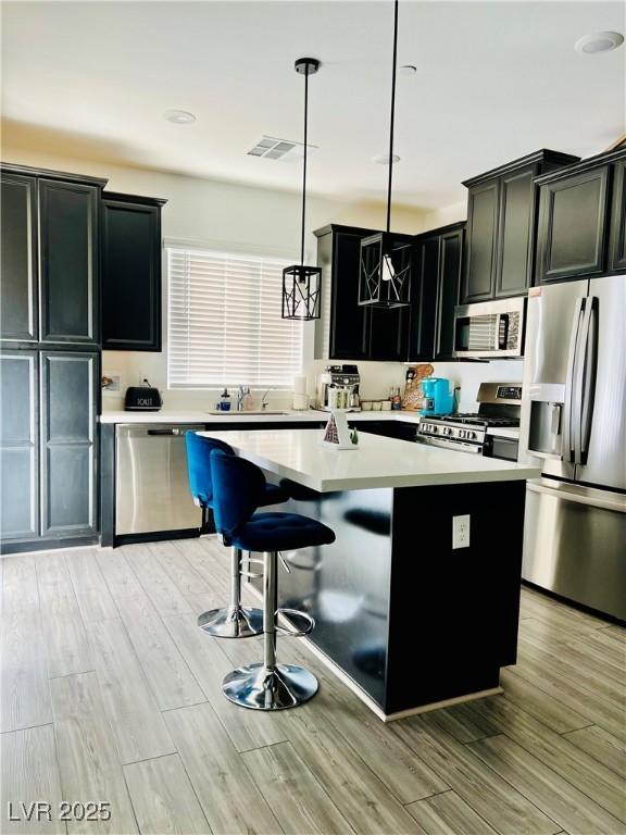 kitchen with light hardwood / wood-style floors, a center island, pendant lighting, sink, and stainless steel appliances