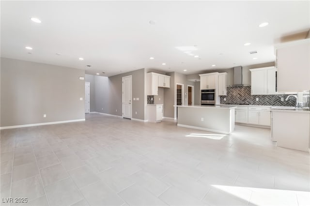 kitchen with a sink, wall chimney range hood, open floor plan, backsplash, and a center island