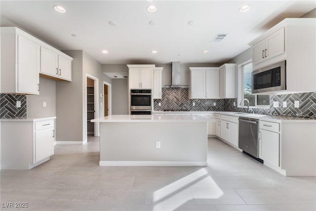 kitchen featuring visible vents, a kitchen island, wall chimney range hood, light countertops, and stainless steel appliances