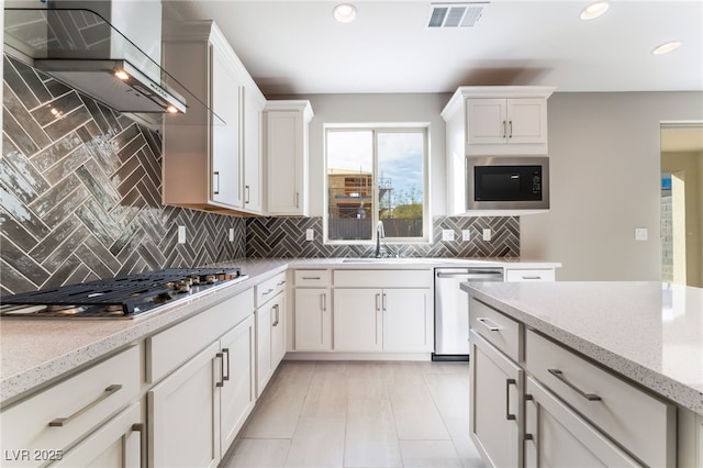 kitchen featuring visible vents, a sink, white cabinetry, appliances with stainless steel finishes, and wall chimney range hood