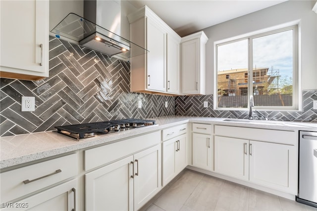 kitchen with a sink, backsplash, appliances with stainless steel finishes, white cabinets, and wall chimney range hood