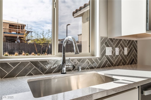 room details featuring backsplash, light stone countertops, white cabinets, and a sink