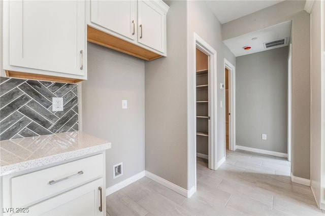 kitchen featuring light stone countertops, visible vents, baseboards, white cabinetry, and backsplash