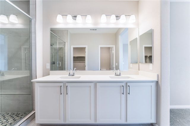 bathroom featuring double vanity, a shower stall, a walk in closet, and a sink