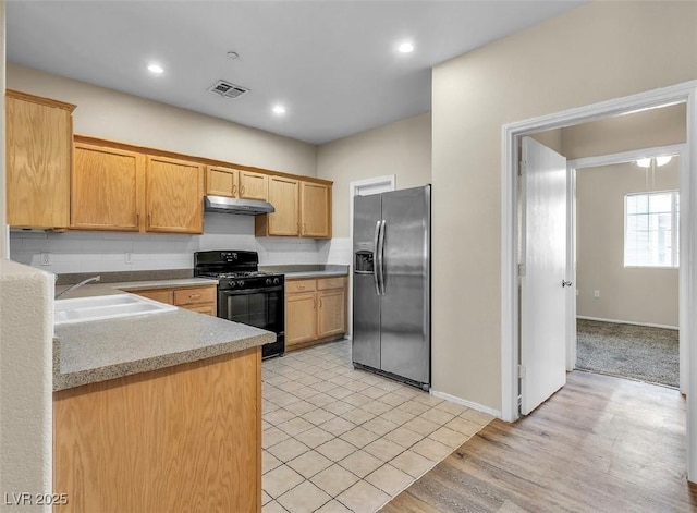 kitchen with stainless steel fridge, visible vents, black gas stove, under cabinet range hood, and a sink