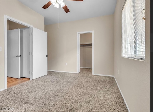 unfurnished bedroom with carpet floors, a spacious closet, baseboards, and a ceiling fan