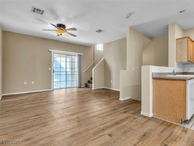 unfurnished living room featuring light wood-style flooring, a sink, visible vents, a ceiling fan, and stairs