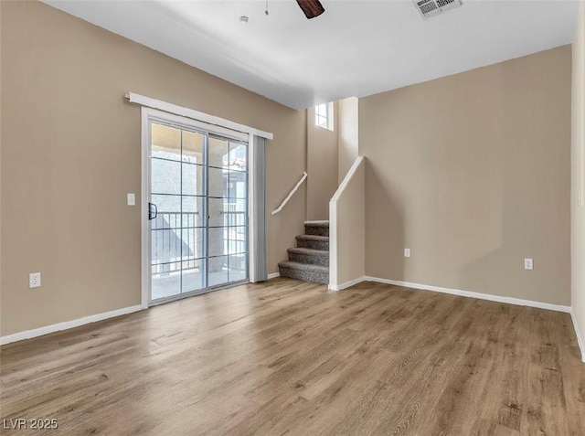 empty room featuring stairs, visible vents, baseboards, and wood finished floors