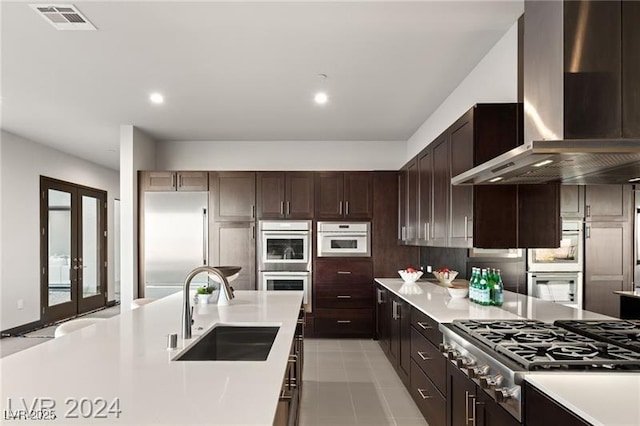 kitchen with appliances with stainless steel finishes, french doors, wall chimney exhaust hood, dark brown cabinetry, and sink