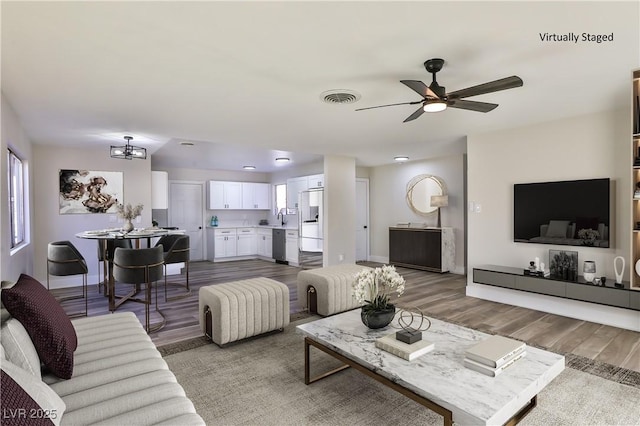 living room with ceiling fan with notable chandelier, light hardwood / wood-style flooring, and sink