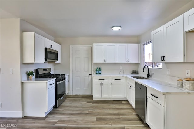 kitchen with stainless steel appliances, light hardwood / wood-style floors, white cabinetry, and sink