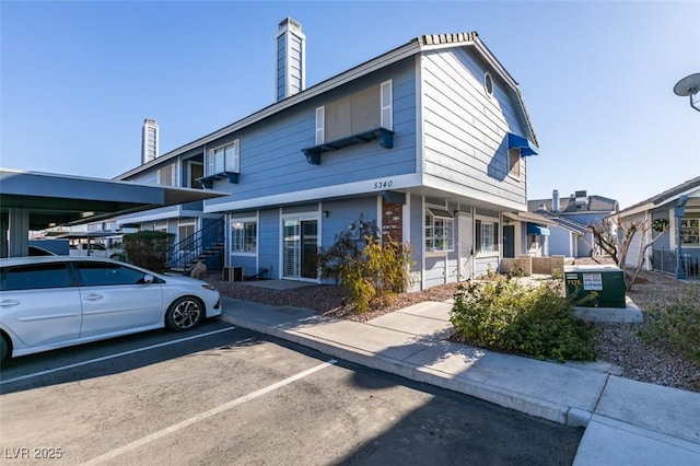 multi unit property featuring a chimney and covered and uncovered parking