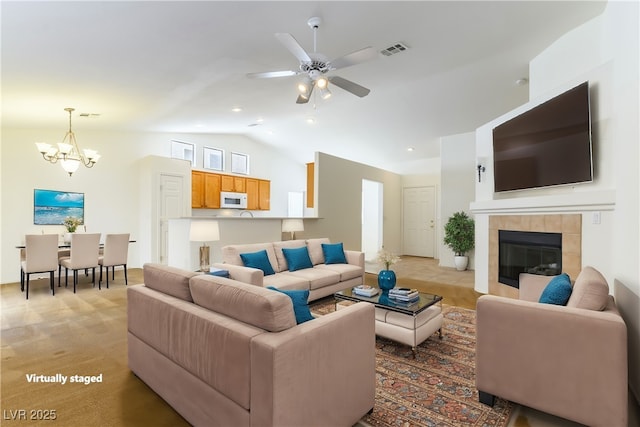 living room featuring ceiling fan with notable chandelier, lofted ceiling, and a tiled fireplace