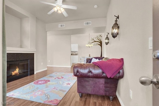 living room featuring ceiling fan, hardwood / wood-style flooring, and a tiled fireplace