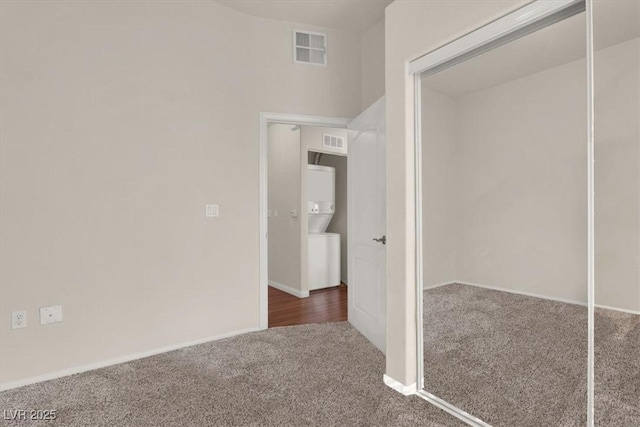 hall with dark carpet and stacked washer and dryer