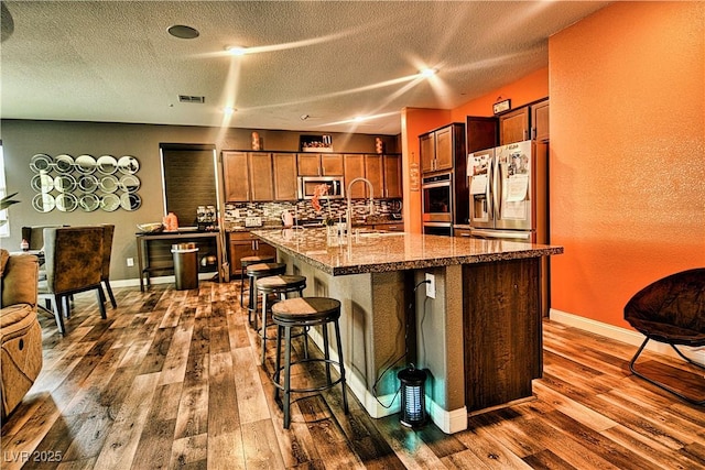 kitchen featuring stainless steel appliances, an island with sink, decorative backsplash, sink, and a breakfast bar area