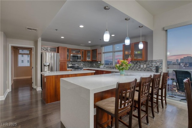 kitchen with appliances with stainless steel finishes, a kitchen bar, sink, hanging light fixtures, and dark hardwood / wood-style floors