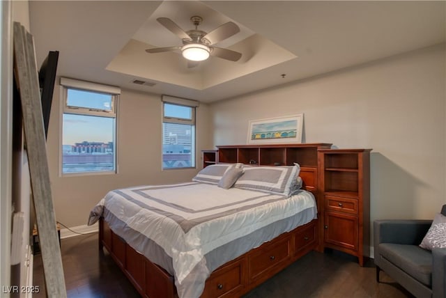 bedroom featuring ceiling fan, dark hardwood / wood-style floors, and a tray ceiling