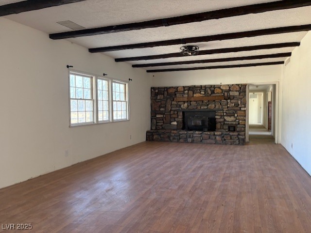 unfurnished living room featuring wood-type flooring, beamed ceiling, and a stone fireplace