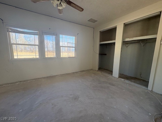 unfurnished bedroom with ceiling fan, two closets, and concrete floors