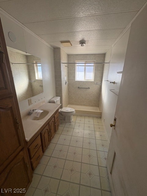 bathroom featuring toilet, ornamental molding, a tile shower, and vanity