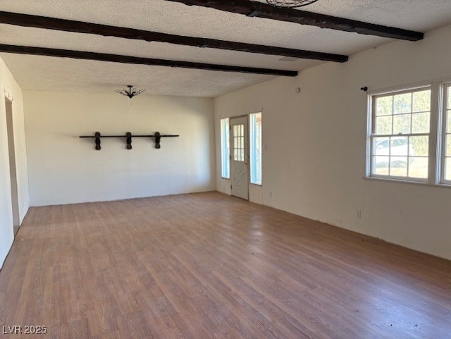 unfurnished room featuring hardwood / wood-style flooring, a textured ceiling, and beam ceiling