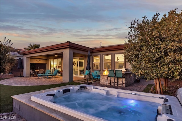 pool at dusk featuring a hot tub, an outdoor bar, an outdoor living space, and a patio area