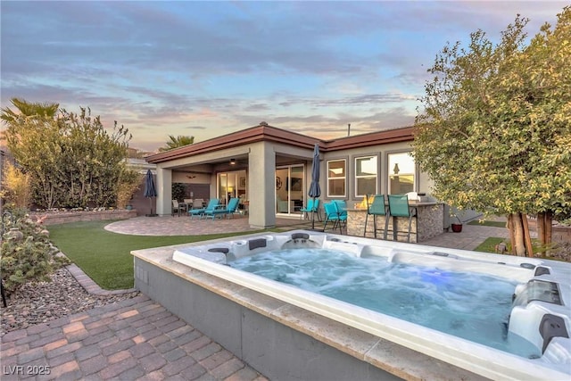 pool at dusk with a patio and an outdoor hot tub