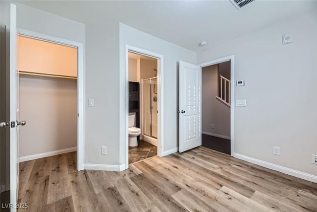 unfurnished bedroom featuring connected bathroom, a closet, a walk in closet, and light wood-type flooring