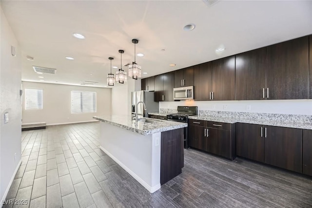 kitchen featuring stainless steel appliances, a kitchen island with sink, pendant lighting, dark brown cabinetry, and sink