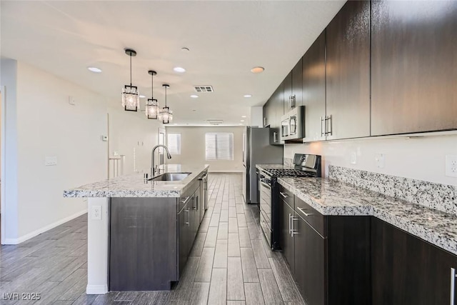 kitchen with gas stove, sink, hanging light fixtures, a kitchen island with sink, and light stone counters