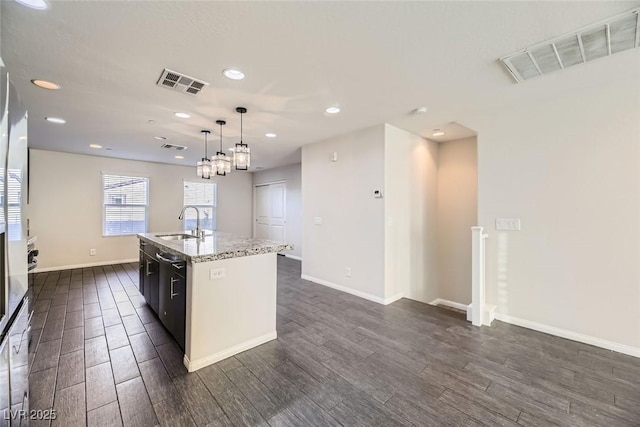 kitchen with light stone countertops, decorative light fixtures, sink, and a kitchen island with sink