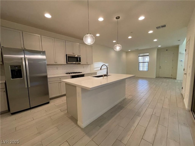 kitchen with pendant lighting, appliances with stainless steel finishes, tasteful backsplash, sink, and a center island with sink