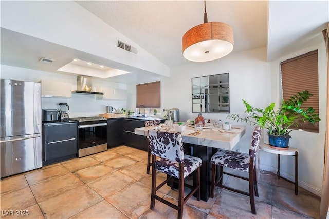 kitchen with appliances with stainless steel finishes, wall chimney exhaust hood, a kitchen breakfast bar, kitchen peninsula, and vaulted ceiling