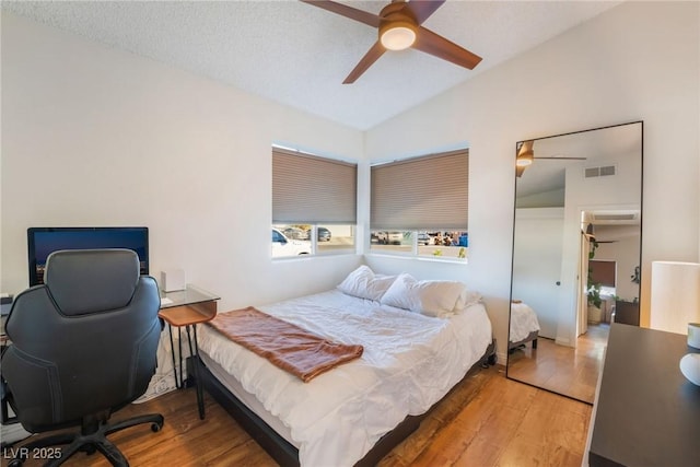 bedroom with ceiling fan, wood-type flooring, vaulted ceiling, and a textured ceiling