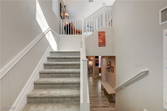 stairway with wood-type flooring and a high ceiling