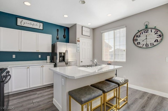 kitchen featuring stainless steel fridge with ice dispenser, a kitchen bar, an island with sink, wood-type flooring, and white cabinets